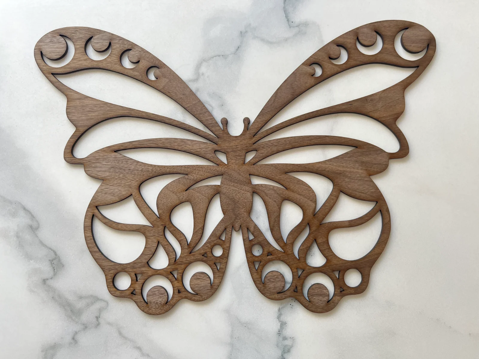 Papillon décoratif en bois de noyer noir, découpé au laser, avec des ailes symétriques ornées de nombreux motifs ajourés et courbes.