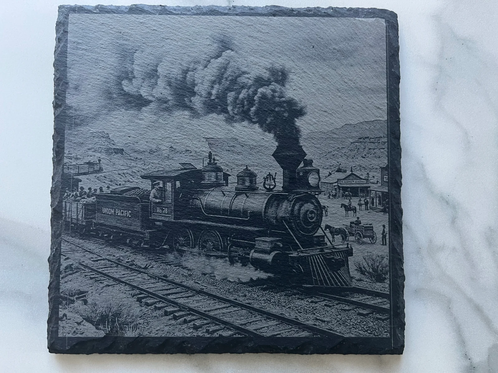 Ardoise noire gravée d’une locomotive à vapeur dans un décor de Far West.